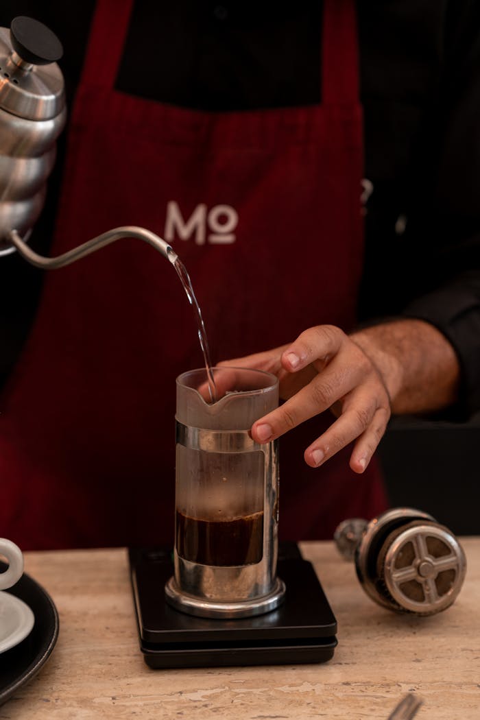 A barista making pour-over coffee using a kettle in a café setting, hands visible.